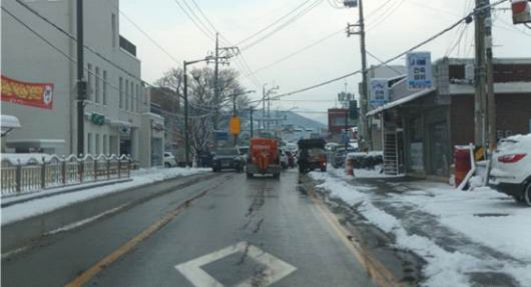 It was snowing until just now and the road surface is frozen · The vehicle directly ahead is a snow-removal vehicle spreading sand on the road · The truck ahead on the right is stopped with its right turn signal on
