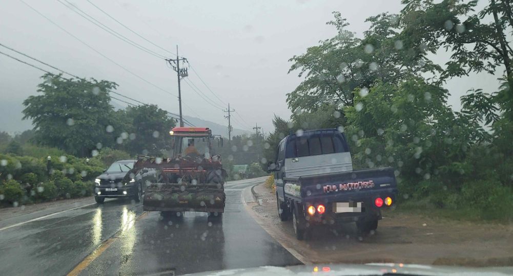 Road with one lane in each direction, curving to the right · Road surface wet from rain · Truck stopped on the right · Tractor stopped while its driver talks with the truck driver on the right