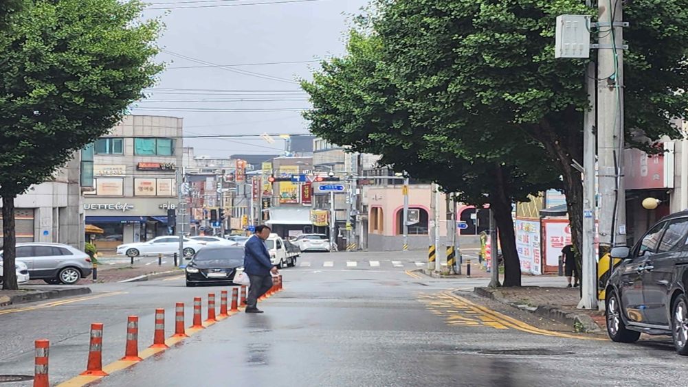 Downhill road with a surface wet from rain · A pedestrian is crossing the roadway · Vehicle traffic light 70 m ahead is red · A passenger car is parked on the right
