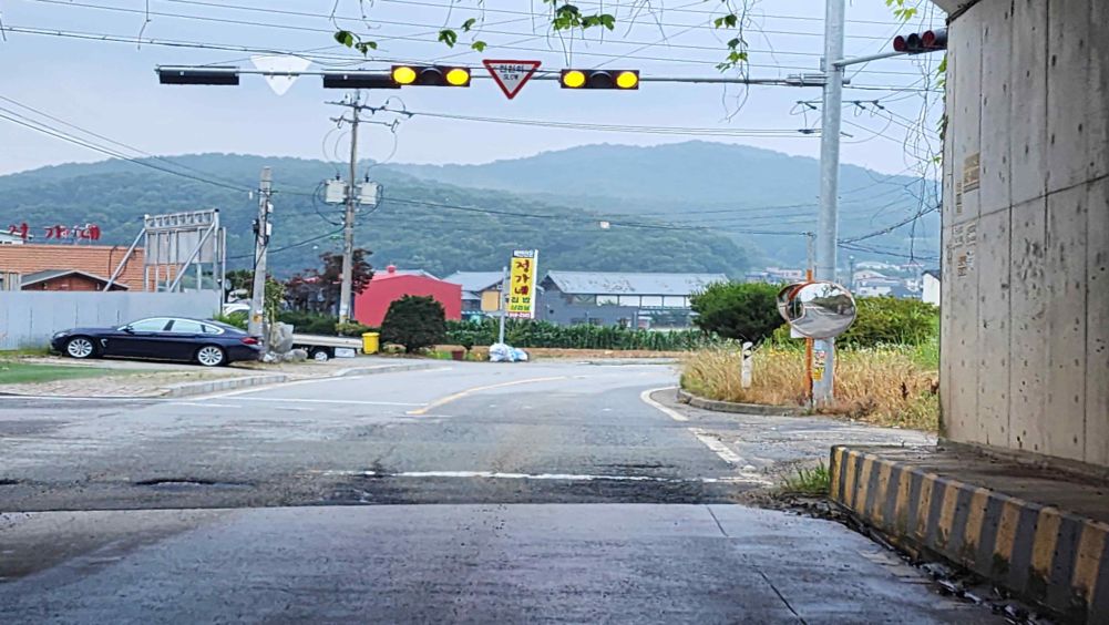 车辆信号灯黄灯闪烁 · 写着“慢行”的安全标志 · 道路右侧有反光镜 · 因下雨路面湿滑的状态 · 路面上到处有坑洞
