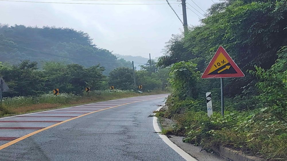 ผิวถนนเปียกเพราะฝนตก · ป้ายจราจรทางด้านขวาของถนน · ถนนขึ้นเนินที่โค้งไปทางขวา